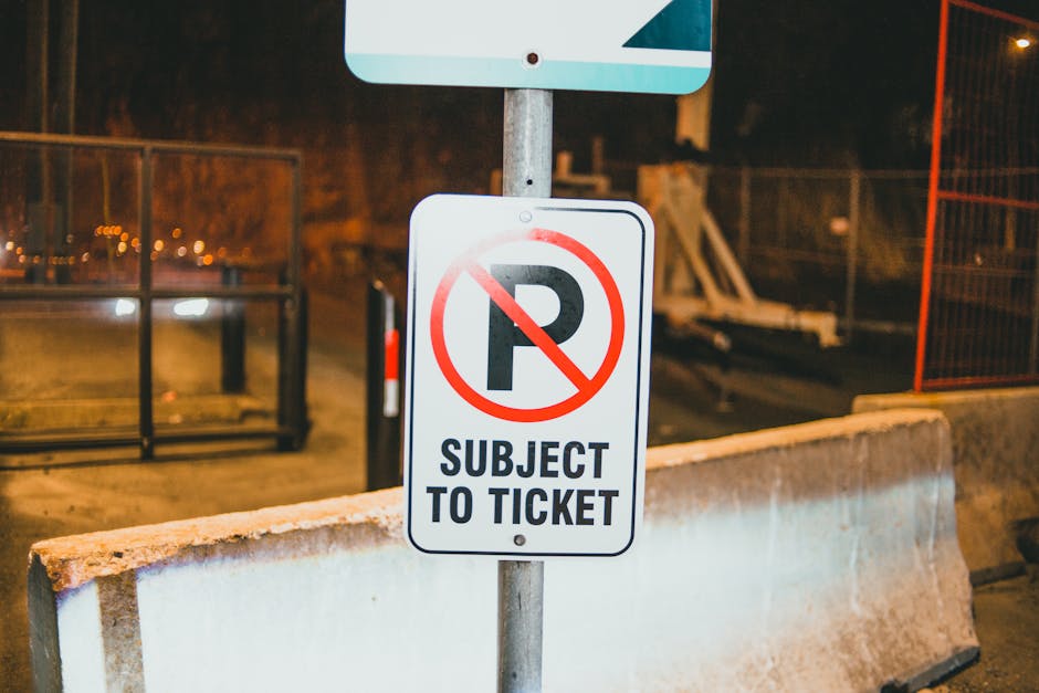 A tall metal street sign post with a rectangular white sign displaying a red circle with a diagonal line crossing out the letter 'P' indicating no parking, and an arrow pointing to the right beneath it. The sign is mounted on the post with two black clips. The background shows a clear blue sky with a slight gradient. This signage is relevant for house removals and relocation services, highlighting parking restrictions in the area, which [COMPANY_NAME] such as Man and Van Barnsbury must consider during home relocation and furniture transport activities on Barnsbury Road.